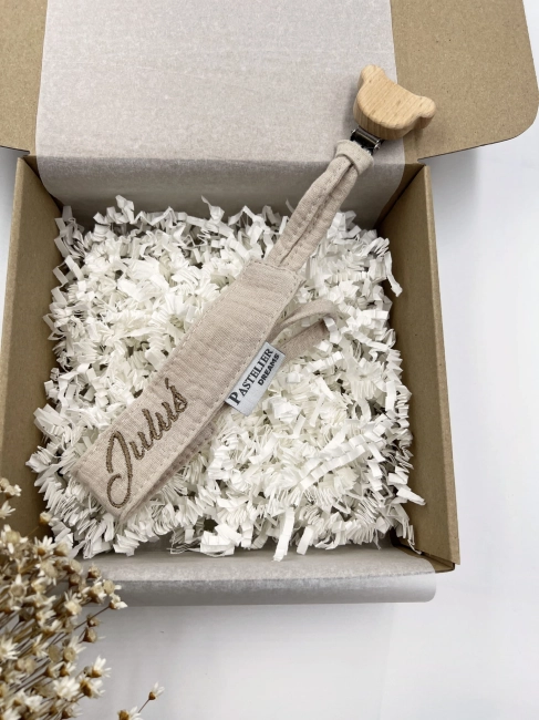 Personalizowana zawieszka do smoczka z haftowanym imieniem i drewnianym klipsem. Praktyczny dodatek do wyprawki niemowlęcej i wyjątkowy prezent dla noworodka.